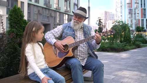 Grandfather Plays Guitar for Granddaughter Outdoors