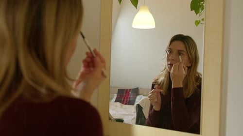 Woman Applying Makeup in the Mirror at Home