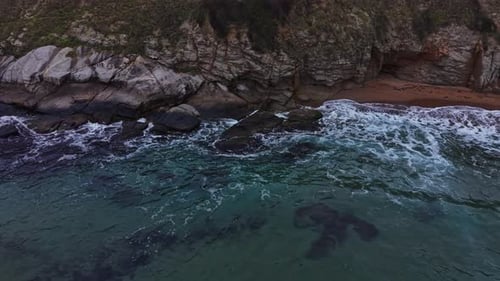 Waves crashing on rocky shore near sandy beach at sunset