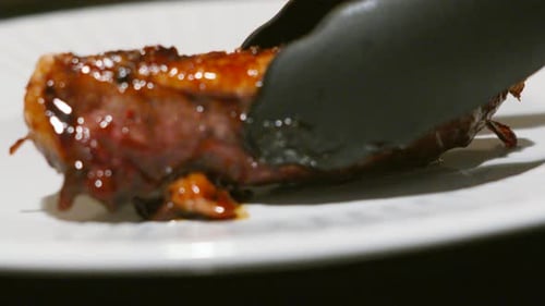 Delicious Duck Fillet Being Plated with Tongs in Kitchen Restaurant Setting
