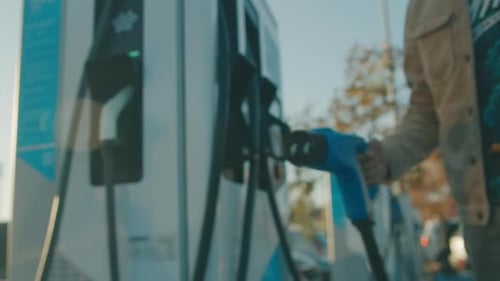 Man connects charging cable to electric car ecological transport in city
