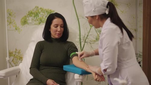 Female Patient Sits in Clinic Chair While Nurse in Gloves Disinfects Her Arm and Applies Tourniquet