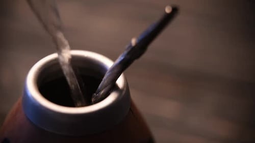 Closeup of Hot Water Being Poured Into a Traditional Mate Cup with a Metal Straw Bombilla A Warm