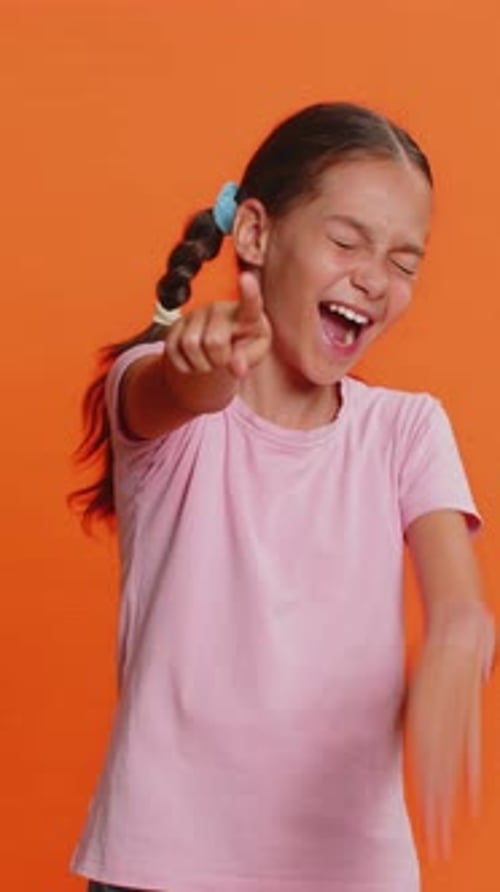 Smiling Girl Points and Laughs on Orange Background
