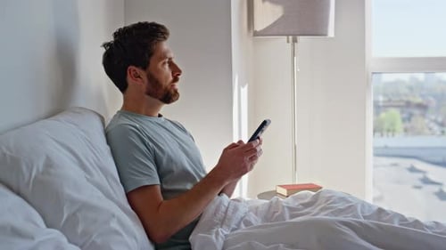 Man Relaxes in Bed Using Mobile Phone