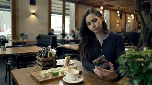 Worried young woman checking her phone anxiously awaiting a date in a cafe