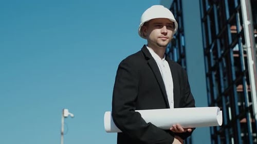 Young Architect Holding Plans Near Building