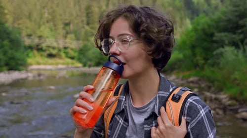 Woman With Backpack, Dressed Clothes For Active Hikes, Drinks Water From Tourist Flask. Girl Drinks