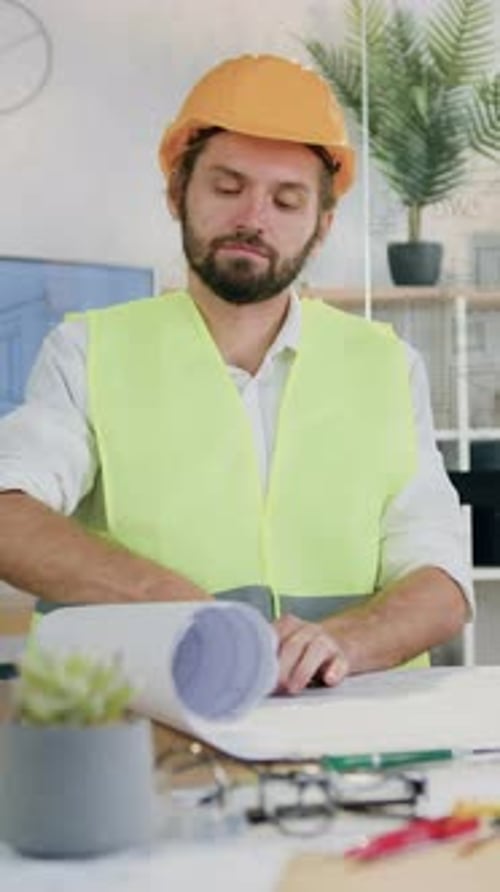 Man in Hard Hat and Vest Examines Blueprints