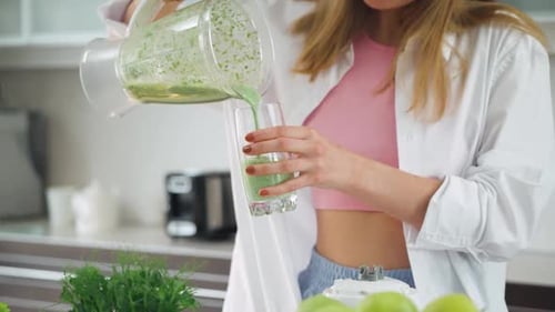 Junge Frau macht Smoothies in der Küche, mischt grünes Gemüse, Zutaten in einem Mixer, gießt