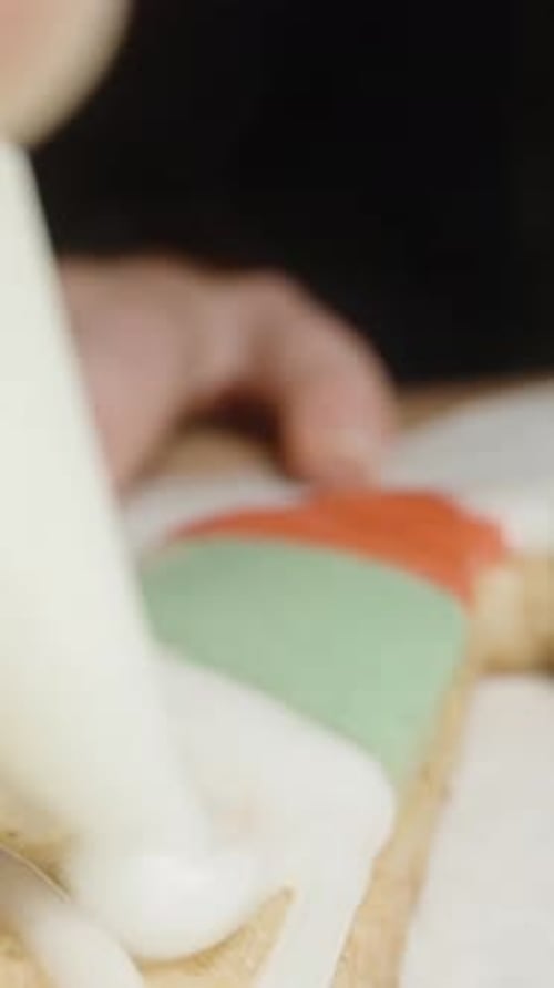 Vertical video. Using white icing, we decorate the gingerbread cookie in the shape of a candy cane.