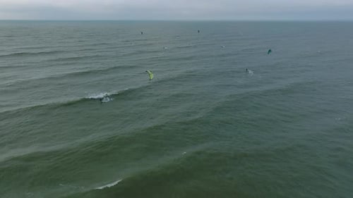 Establishing aerial view of a group of people engaged in kitesurfing, overcast winter day, high wave