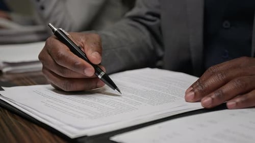 Hände eines schwarzen männlichen Anwalts beim Korrekturlesen und Unterzeichnen des Dokuments bei der Sitzung