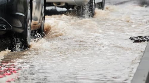 Cars Driving on Flooded Street Splashing Muddy Water After Heavy Rainfall