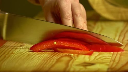 Knife cuts the red pepper in kitchen on wooden board. Close up.
