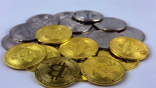 Silver and gold bitcoin rotate on white surface