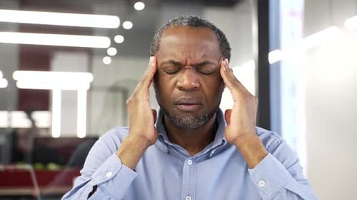 African american businessman suffering from headache sitting at workplace in office. Upset black man