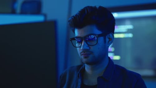 Vista aproximada de jovem programador de óculos em escritório azul escuro