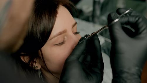 Interior de un estudio de piercings: el maestro de piercings hace un piercing para una niña, piercing para el tabique nasal