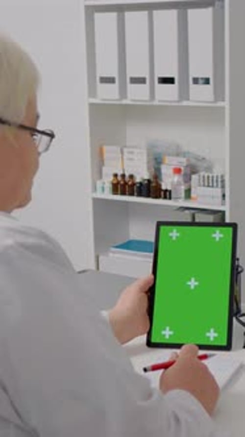 Vertical Screen Senior medical worker watches green screen chroma key vertical tablet.