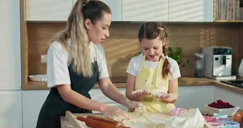 Linda jovem irmã loira mais velha ensinando o pequeno a amassar massa em uma cozinha moderna e iluminada