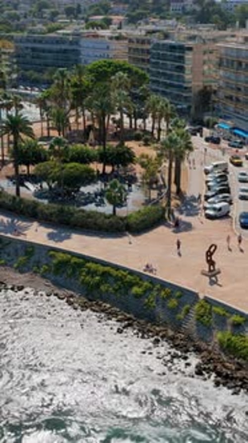 Aerial drone view of Antibes seafront promenade, curved walkway lined with palm trees, overlooking t