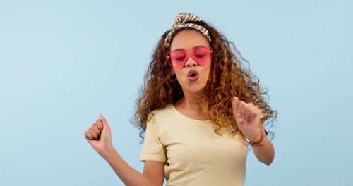 Happy, dancing and young woman in a studio with funky, cool and stylish sunglasses listening to