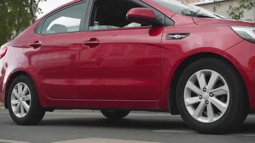 Red Car Sedan Drives on Empty Street Passing Old Buildings