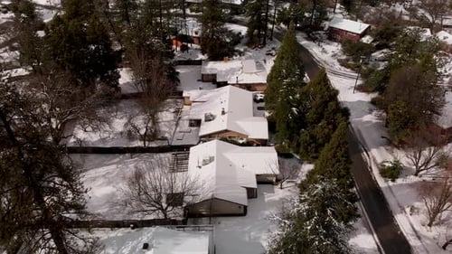 Aerial Shot of Small Rural Town, Rooftops Covered in Snow Surrounded by Pine Trees in Winter