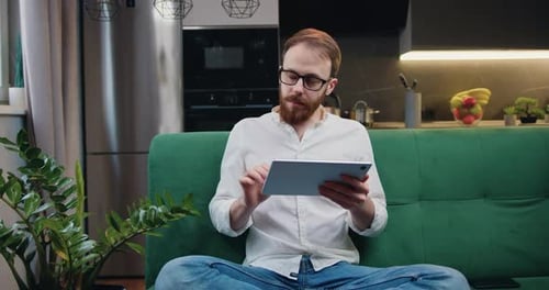 Man Using Tablet on Green Couch in Apartment