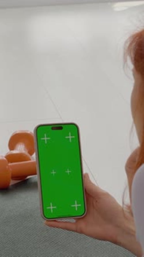 Vertical video Woman checks smartphone during gym break while sitting on exercise mat