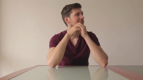 Young man sitting at table being indecisive about a choice and thinking hard, medium close-up shot f