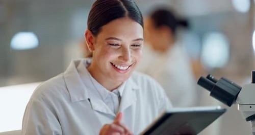 Young Woman Using Tablet and Microscope in Lab