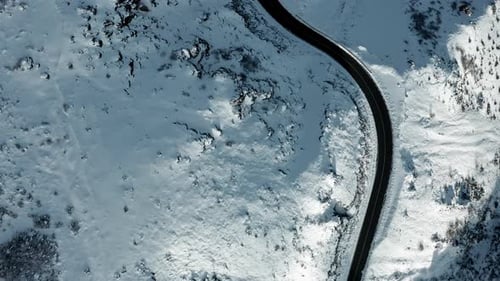 A curvy road snaking through a snow-covered landscape, offering a stark contrast, aerial view