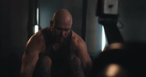 Closeup Shot of a Bearded Man in a Tank Top Exercising on a Rowing Machine in a Contemporary Gym