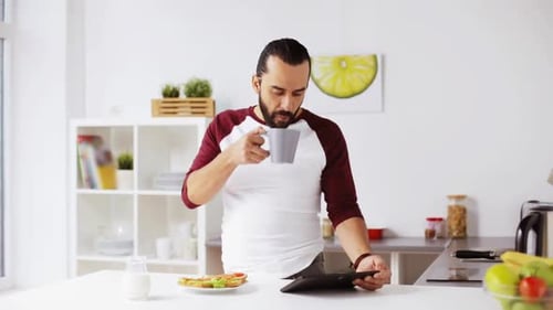 Man Using Tablet and Drinking Coffee in Kitchen