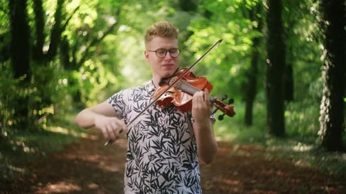 Medium shot of young man playing the violin in beautiful dreamy forest