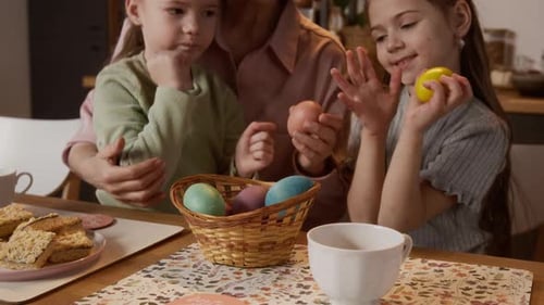 Playful Little Girls Putting Colorful Easter Eggs in Basket