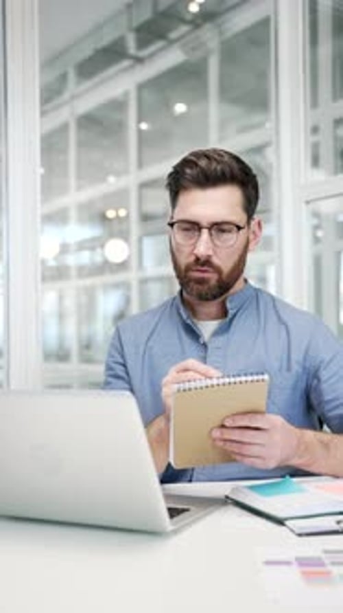 Man Taking Notes While Working at Computer