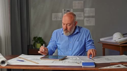 An Architect Sits in an Office at a Desk with Blueprints