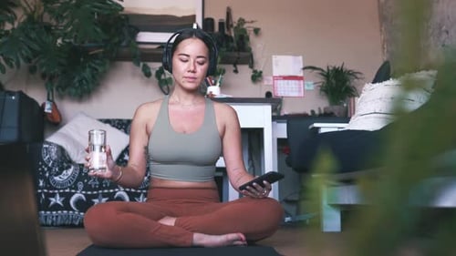 Woman Drinking Water and Using Phone on Yoga Mat