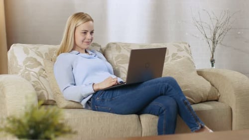 Woman Working on Laptop While Relaxing on Couch