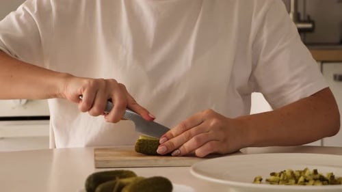 In einer hellen Küche schneidet eine Frau gekonnt eingelegte Gurken in feine Stücke. Nahaufnahme
