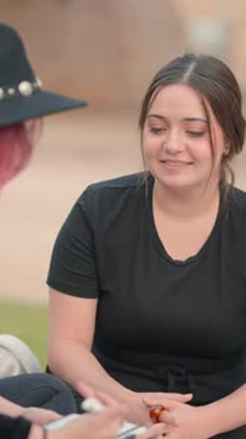 Two Caucasian Young Women Chatting While Sitting on the Grass Medium Close Up