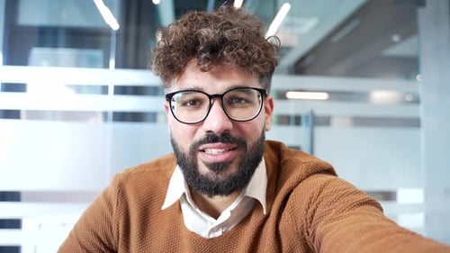 POV Smiling businessman talking on video call using a phone in the office.