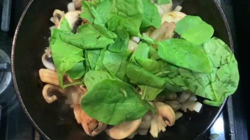 Cooking mushrooms, onions, and green spinach using a cast iron skillet. Healthy diet foods.