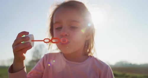 Authentic shot of little girl blowing soap bubbles in spring park on a sunny day.