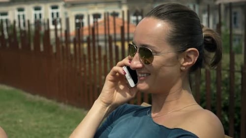 Young, Pretty Woman Talking on Cellphone Sitting in Garden in City 30s