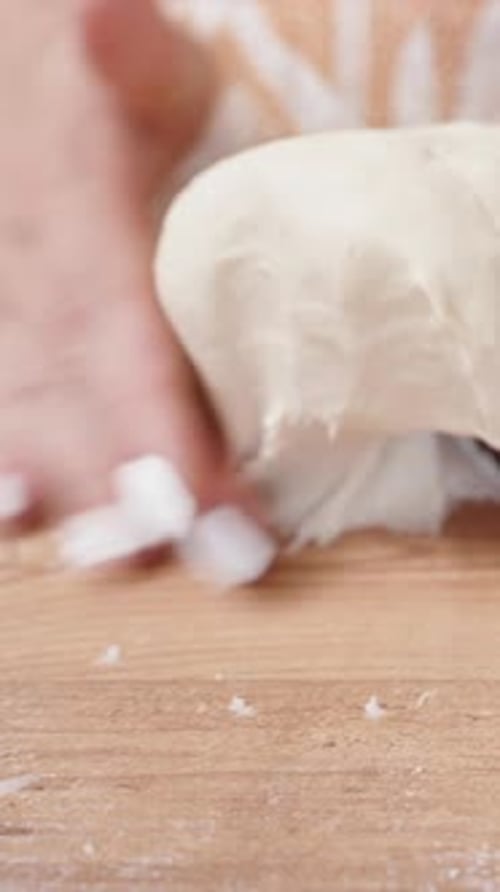 Vertical video. A woman lifts the lump of dough from the table and transfers it into a blue bowl.