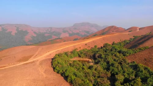 Drone moving sidewards following a mud path on a hill with rolling hills in the background